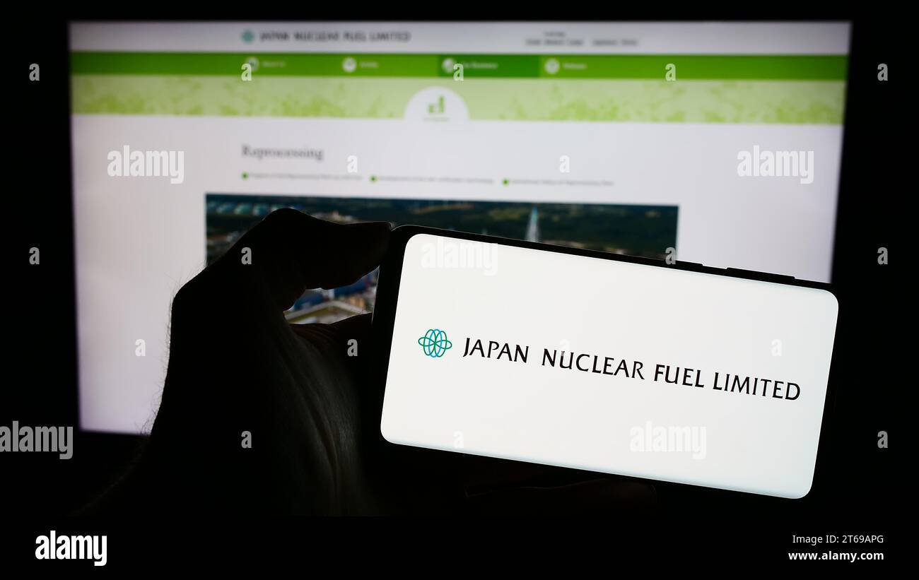 Person, die ein Mobiltelefon mit dem Logo des japanischen Energieunternehmens Japan Nuclear Fuel Ltd. Hält (JNFL) vor der Webseite. Schwerpunkt auf dem Display des Telefons. Stockfoto