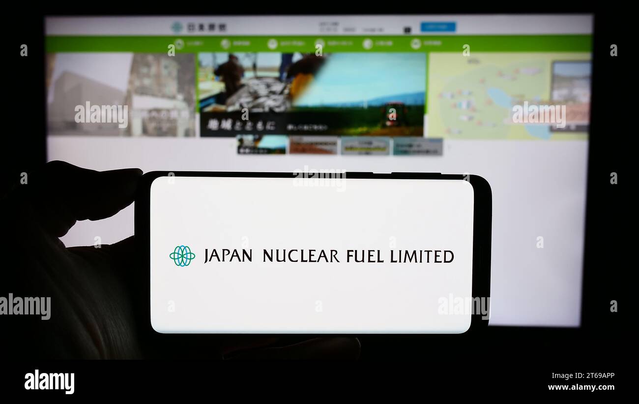 Person, die ein Mobiltelefon mit dem Logo des japanischen Energieunternehmens Japan Nuclear Fuel Ltd. Hält (JNFL) vor der Webseite. Schwerpunkt auf dem Display des Telefons. Stockfoto