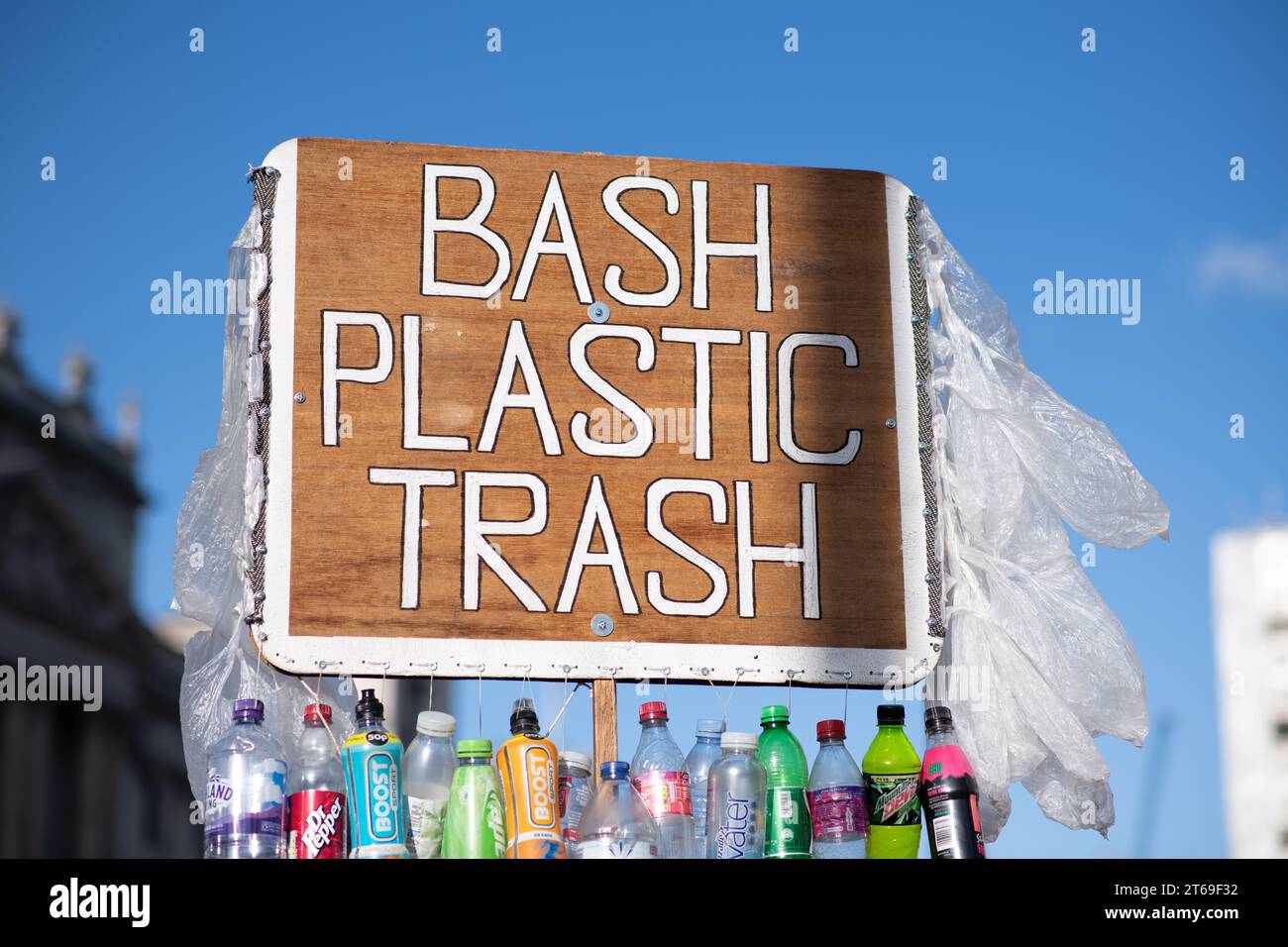 Auf einem Schild, das hoch über einem blauen Himmel steht, steht „BASH PLASTIC MÜLLEIMER“ mit einer Linie aus Plastikflaschen darunter Stockfoto
