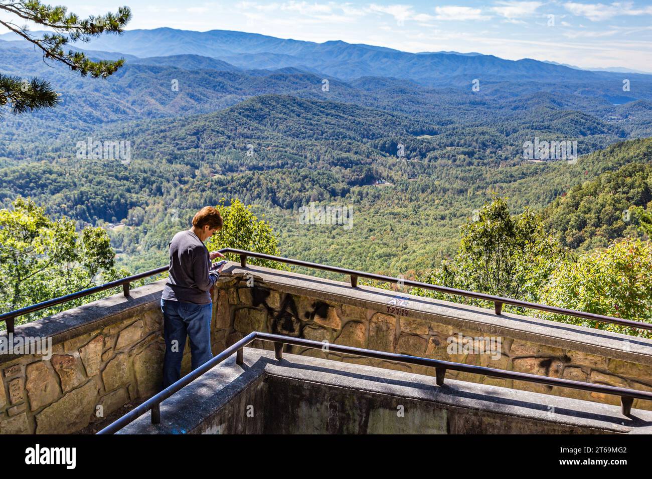 Eine Frau, die auf ein Handy blickt, auf einem malerischen Aussichtspunkt am Foothills Parkway in der Nähe des Wears Valley, Tennessee, im Great Smoky Mountains National Park Stockfoto