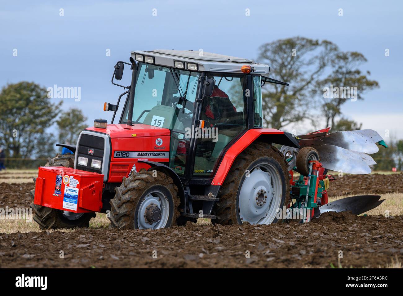 Die Abbildung zeigt einen roten Traktor, der den Boden pflügt, während verschiedene landwirtschaftliche Arbeitsgeräte verwendet werden, um einen Einblick in die Landwirtschaft zu erhalten Stockfoto