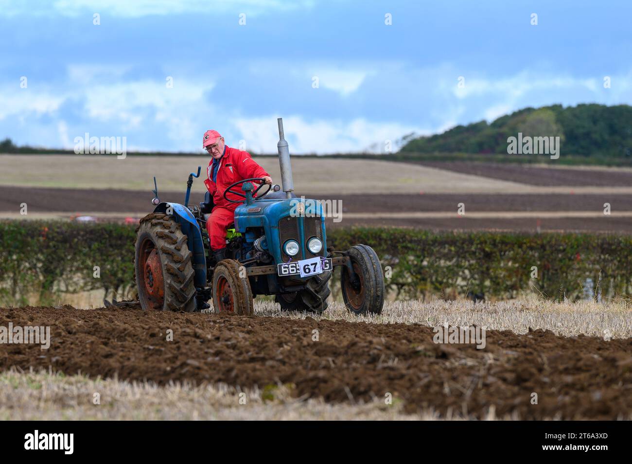 Ein Landwirt fährt einen roten Traktor auf einem weiten, offenen Ackerfeld Stockfoto