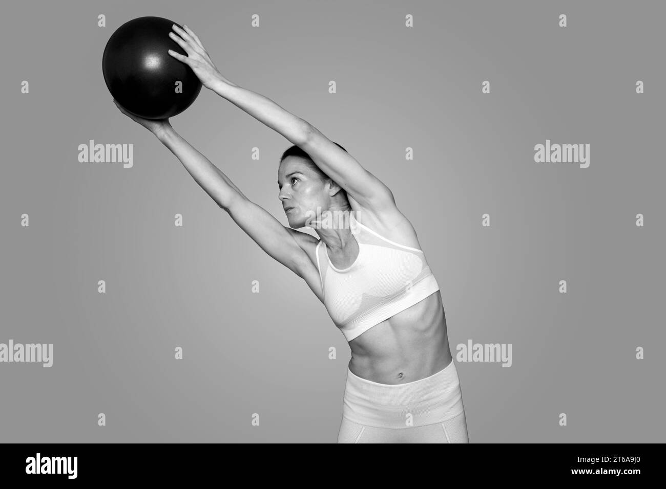 Frau, die einen Pilateball hält und sich dehnt, schwarz-weiß. Stockfoto