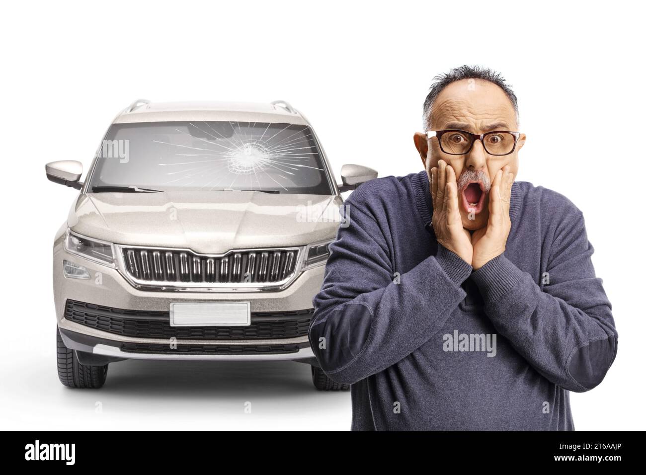 Schockierter reifer Mann, der sein Gesicht vor einem Fahrzeug mit gebrochener Windschutzscheibe auf weißem Hintergrund hält Stockfoto