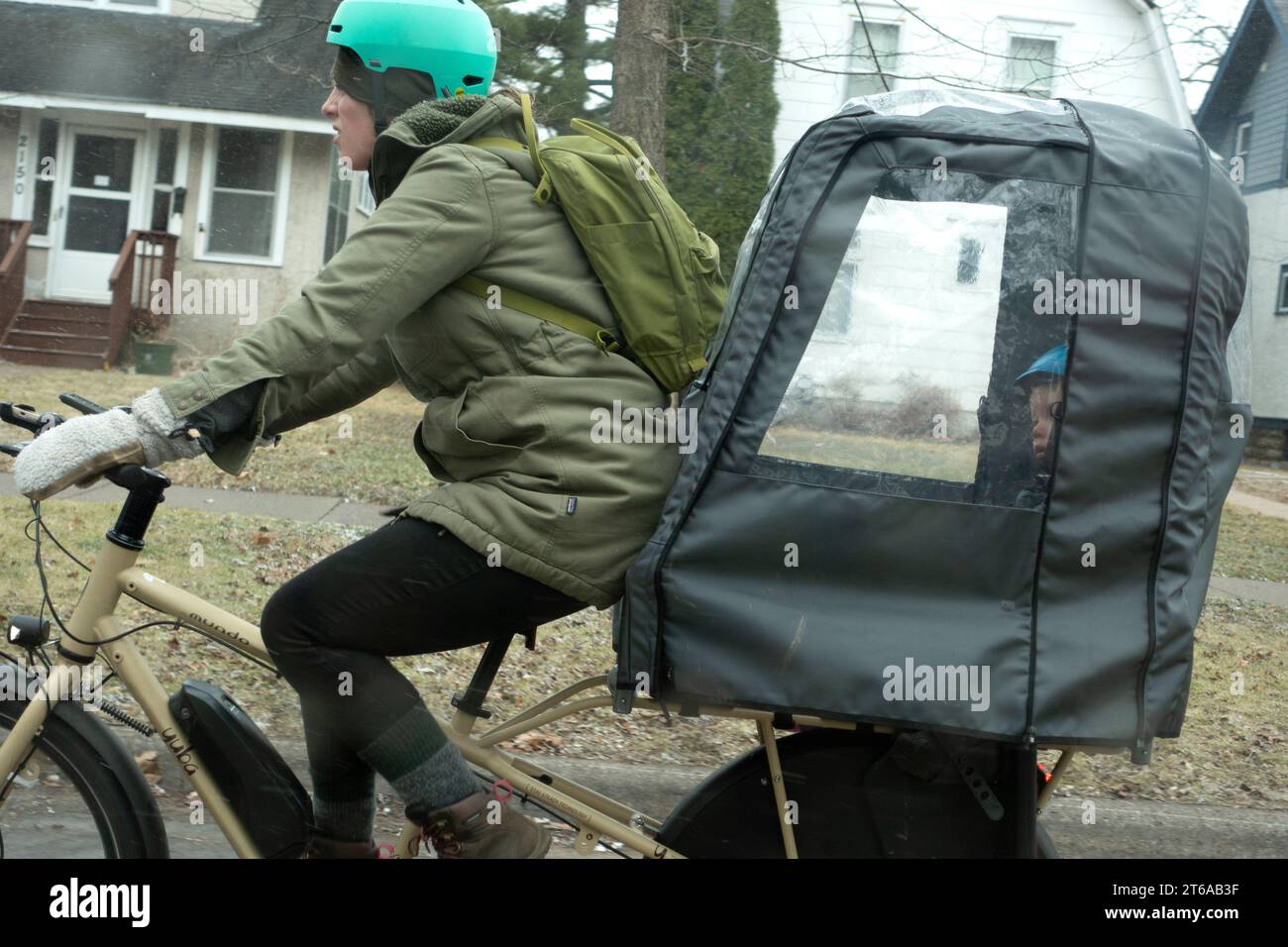 Helm-Mutter, die ihr Kleinkind in einer Tasche für eine Fahrradtour an einem regnerischen Tag mitnimmt. St. Paul Minnesota MN USA Stockfoto