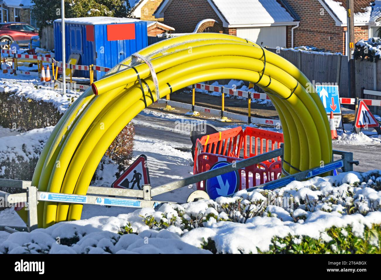 Winter Schnee und vereiste Straßen schließen Straßenarbeiten in einem Wohndorf große gewickelte gelbe Gasleitung ab, um alte gusseiserne Essex England UK zu ersetzen Stockfoto