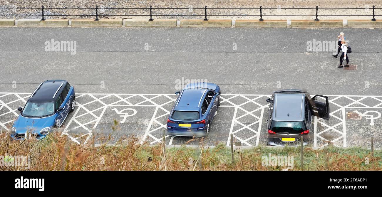 Blaue Parkplatzhalter für Behinderte, Parkplätze aus der Vogelperspektive auf weiße Straßenmarkierungen mit Rollstuhlsymbol und Schlupfwinkel an der Strandpromenade Norfolk UK Stockfoto