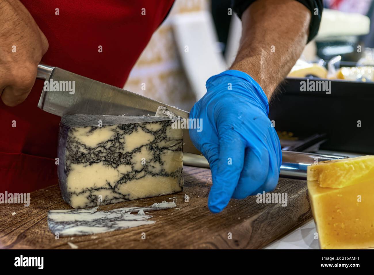 Verkäufer schneidet Schimmelkäse auf Holzbrett. Käserei. Stockfoto