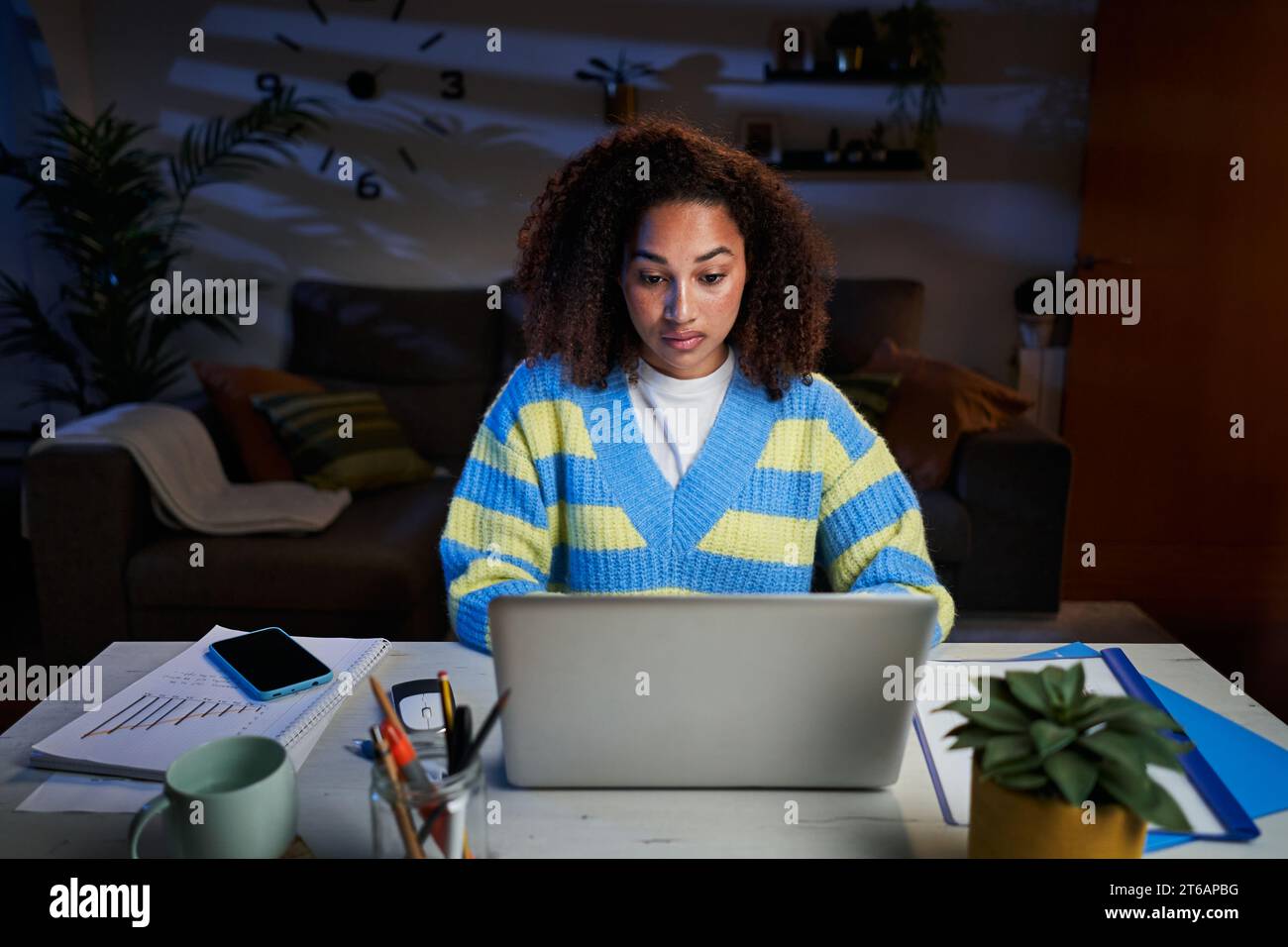 Junge schöne Lateinfrau, die sich nachts mit Laptop im Wohnzimmer konzentriert. Afro-Studentin. Stockfoto