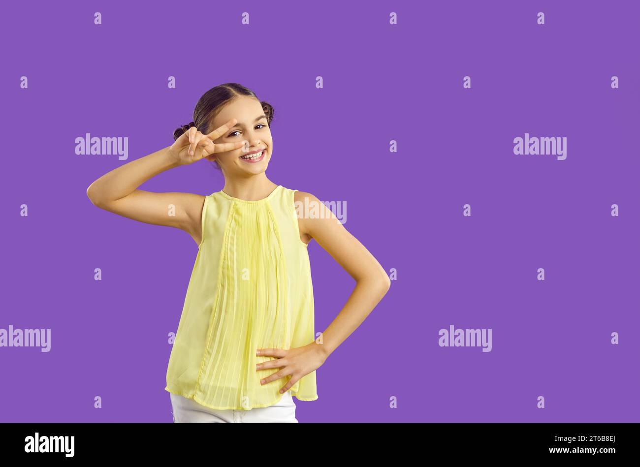 Studio-Porträt des niedlichen lächelnden Mädchens, das V-Schild in der Nähe des Auges auf lila Hintergrund hält. Stockfoto