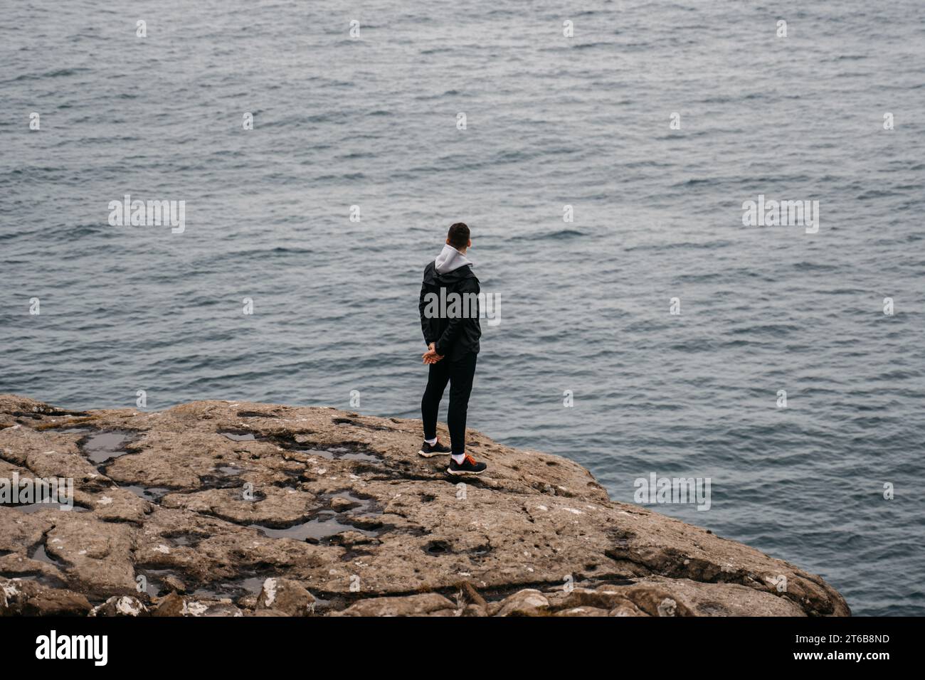 Ein kaukasischer Mann in seinen frühen 30ern steht auf einem Felsvorsprung mit Blick auf das Wasser Stockfoto