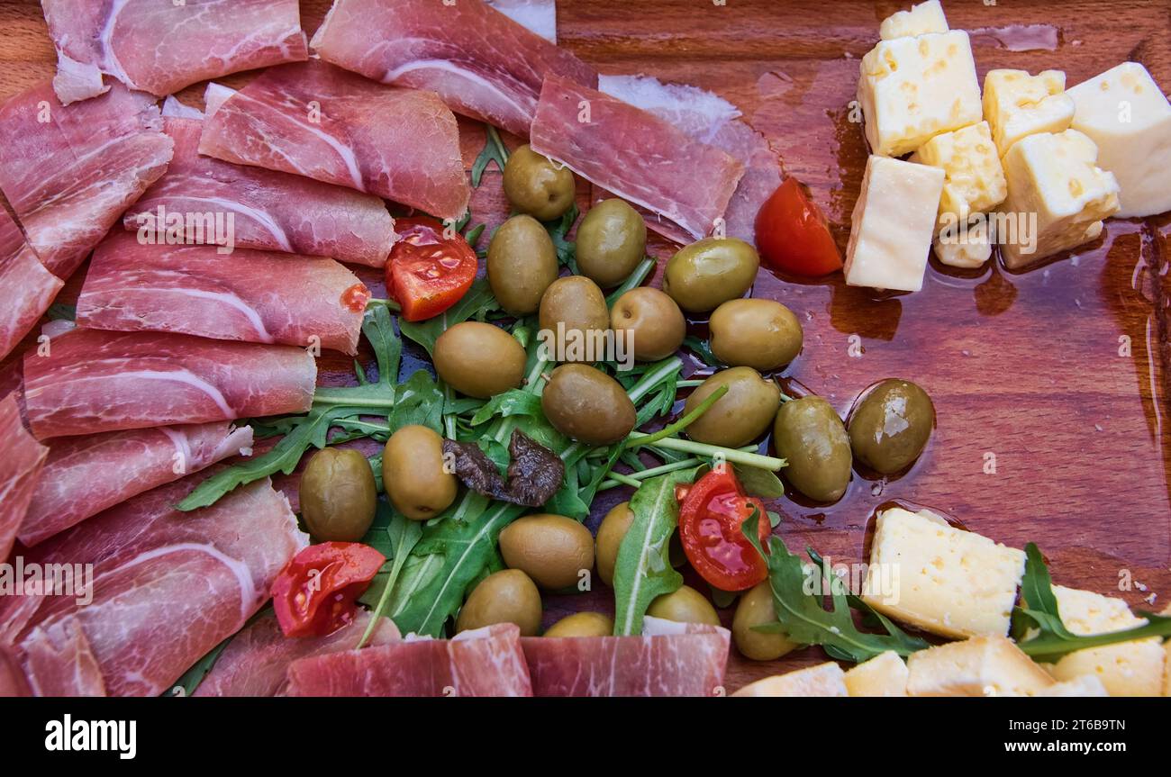 Köstliche Antipasto-Feier mit Rucola, Oliven, gesalzenem Fleisch, frischem Hartkäse auf einem Holzbrett. Stockfoto