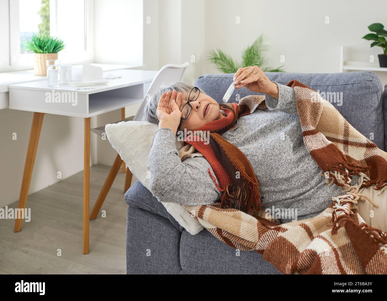 Ungesunde ältere Frau, die zu Hause auf dem Sofa liegt, mit hohem Fieber und starken Kopfschmerzen. Stockfoto