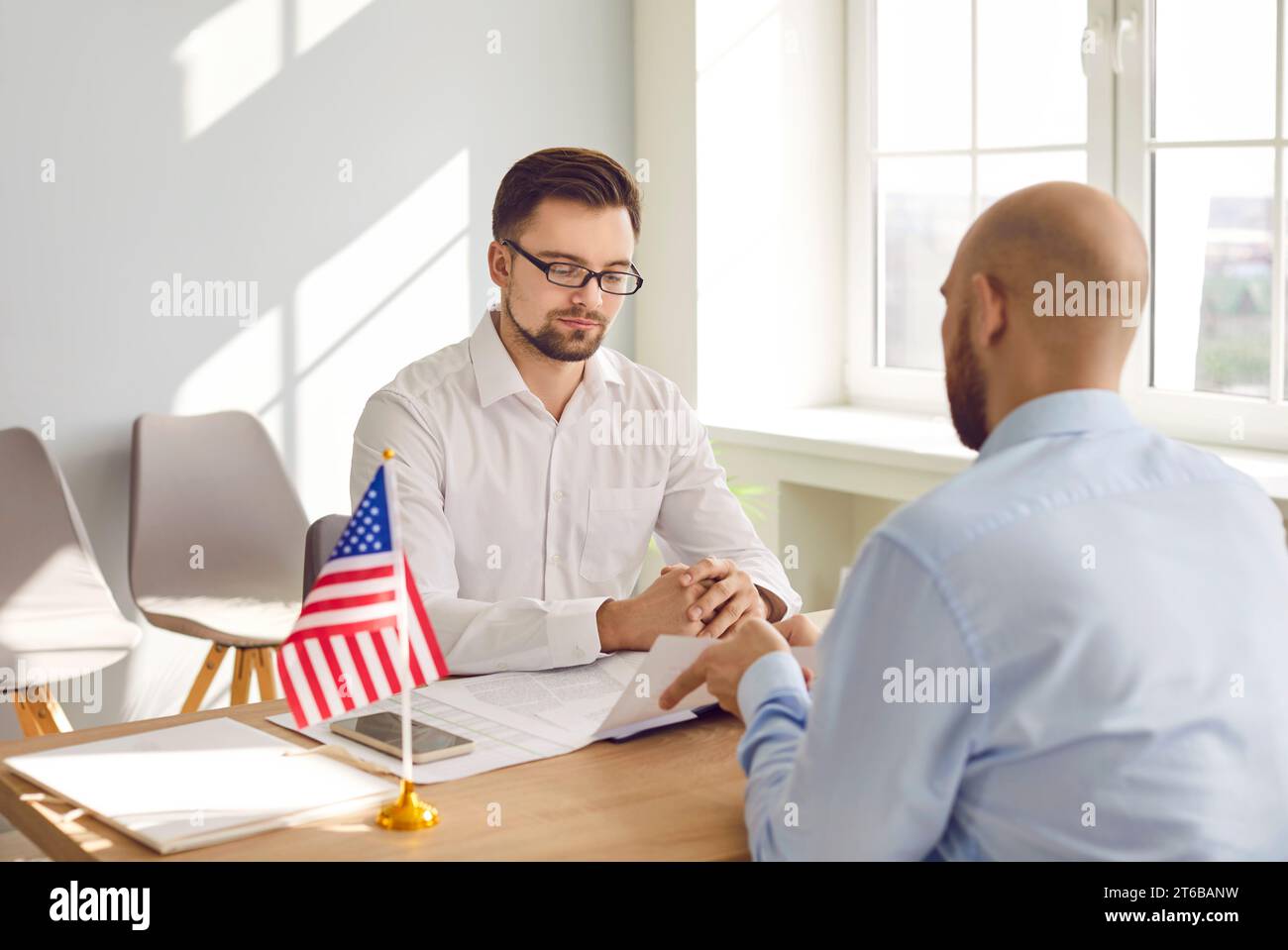 Mann im US-amerikanischen Konsulat, der sich das Visumantragsformular eines jungen Mannes ansieht Stockfoto