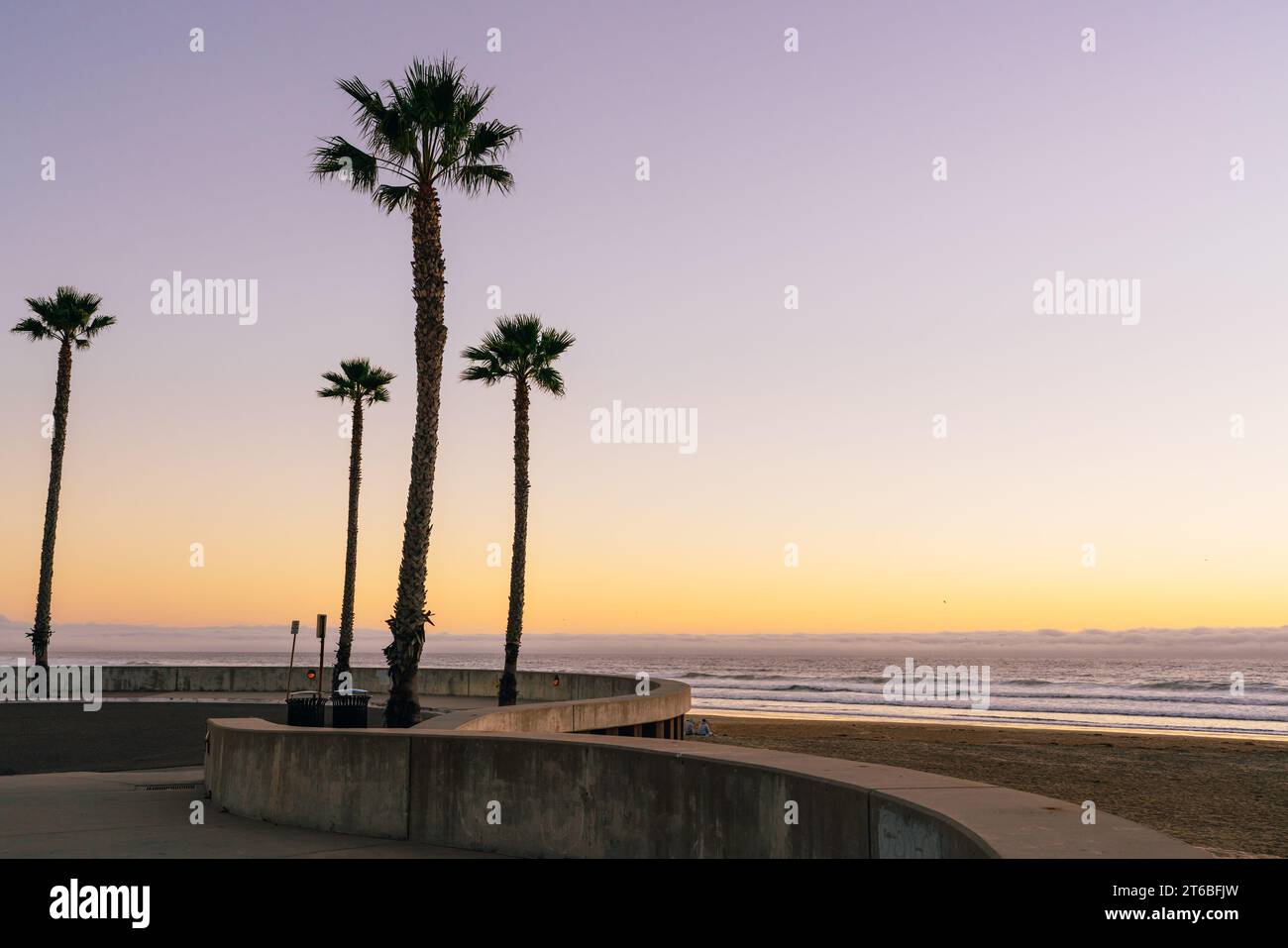 Ein faszinierender rosafarbener Sonnenuntergang taucht den Strand in warme Farbtöne und strahlt einen ruhigen Glanz über die Palmen aus, die sich vor dem pulsierenden Himmel bilden Stockfoto