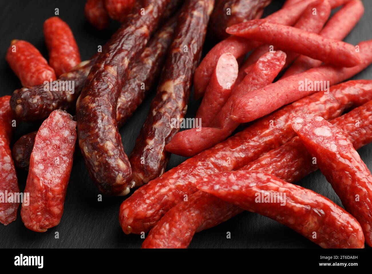 Verschiedene dünne trocken geräucherte Würstchen auf schwarzem Tisch, Nahaufnahme Stockfoto