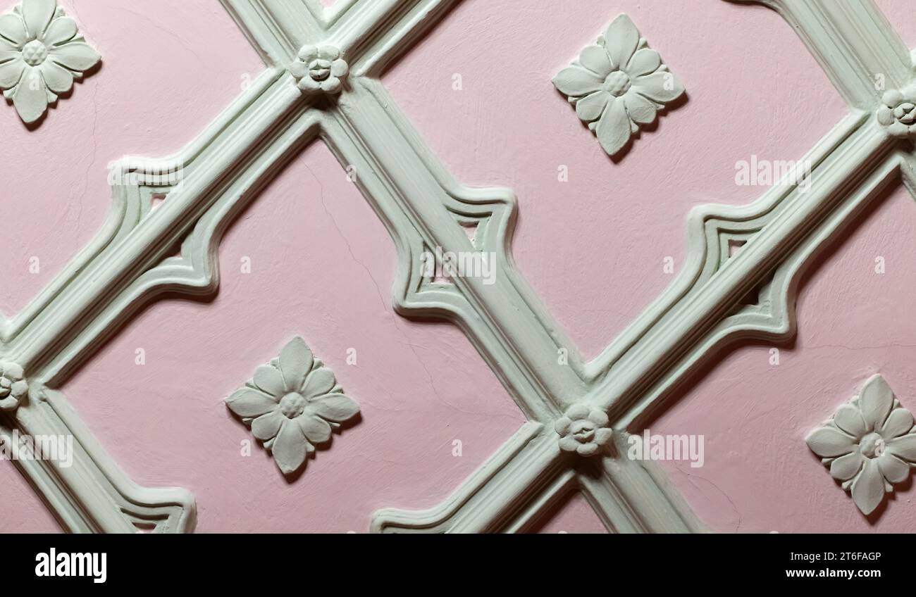Deckenelemente. Hellgrüner Gipsbalreliefmuster über rosa Hintergrund, Nahaufnahme. Abstrakte Vorlage für klassische Architektur Stockfoto