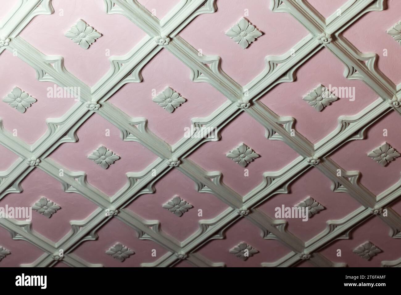 Details zur Deckengestaltung. Hellgrünes Basreliefmuster aus Gips auf rosa Hintergrund, abstrakte Vorlage aus klassischer Architektur Stockfoto