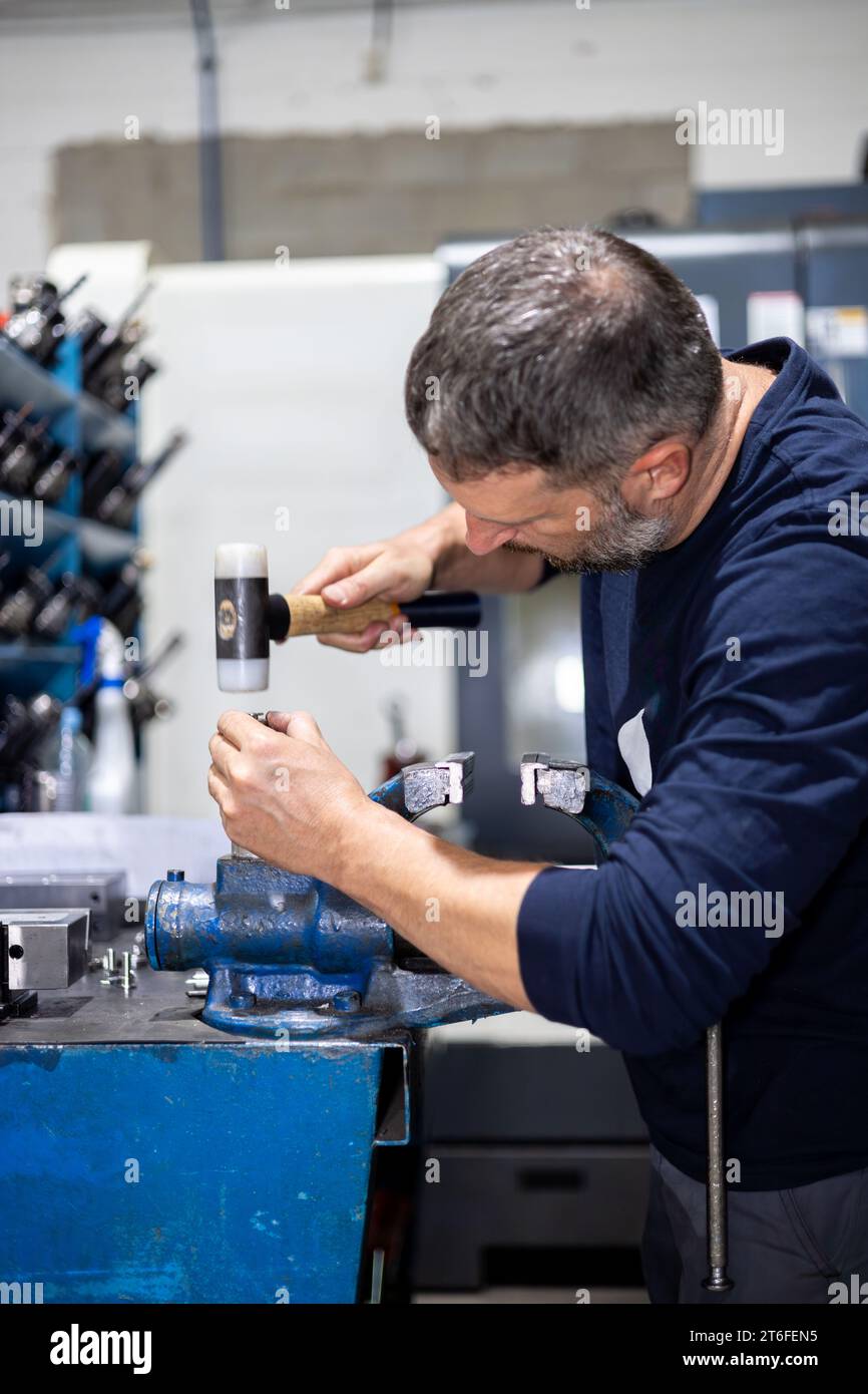 Professioneller Mann, der in einer Metallwerkstatt mit Hammer an einem Stahlstück arbeitet. Industriemechaniker und Reparaturen Stockfoto