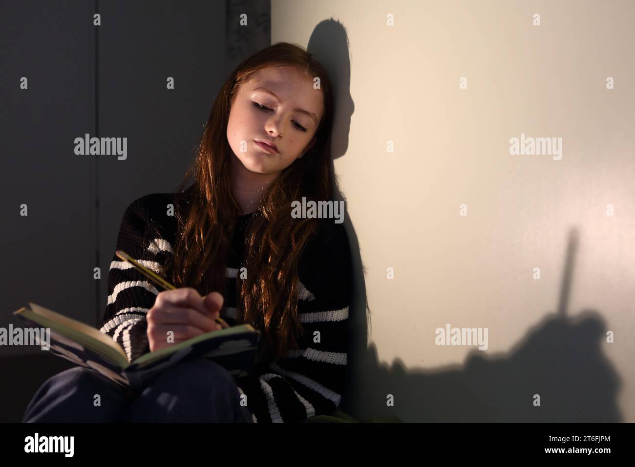 Teenager-Mädchen macht Notizen mit einem Bleistift in einem Notizbuch, denkt darüber nach, was man schreiben soll, Schatten an der Wand des Notizbuchs und Bleistift Teenager schreiben Stockfoto