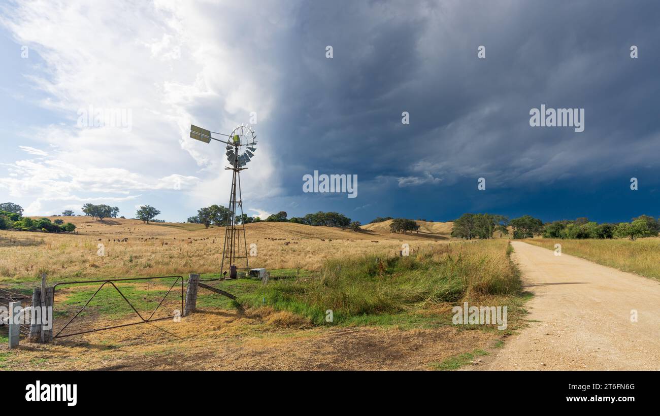 Ein stürmischer Himmel über einer Windmühle und einem Tor zur Farm in einer ländlichen Umgebung in Yapeen in Central Victoria, Australien Stockfoto