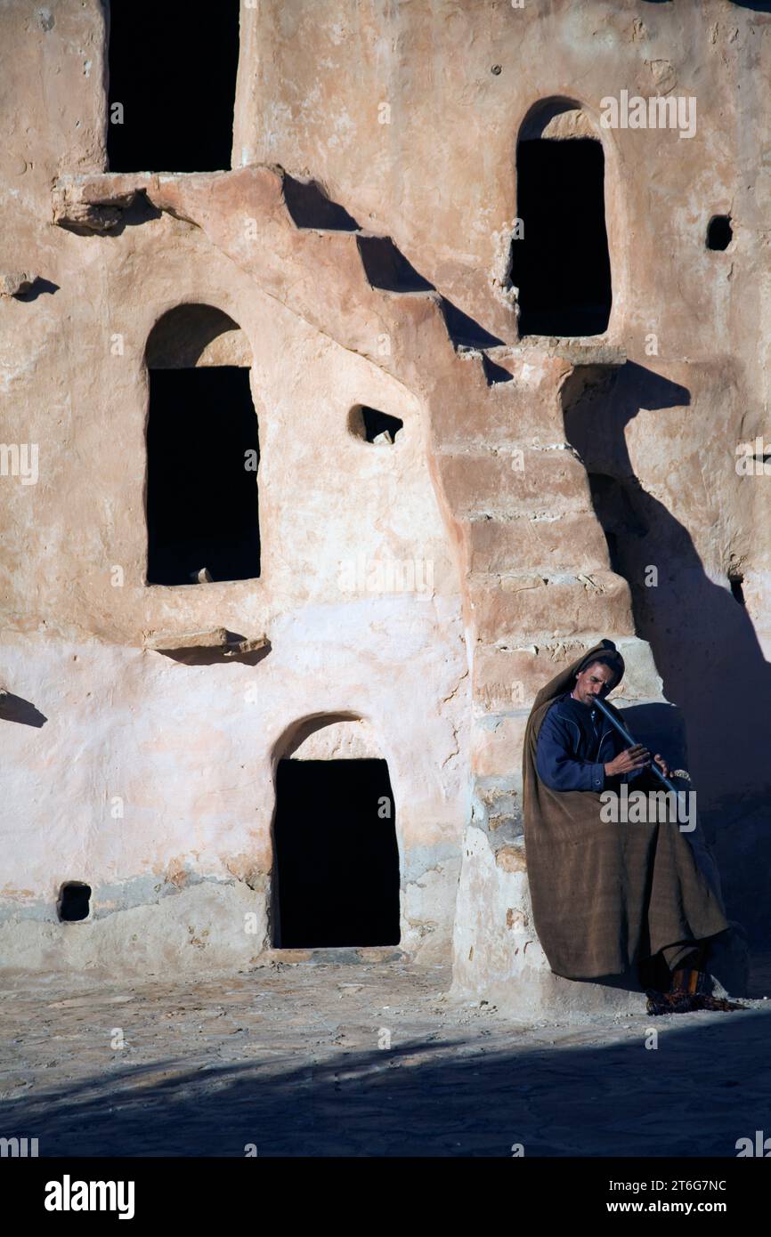 Ein Musiker in traditioneller Kleidung spielt eine arabische Flöte im Festungsspeicher von Ksar Ouled Soltane. Stockfoto