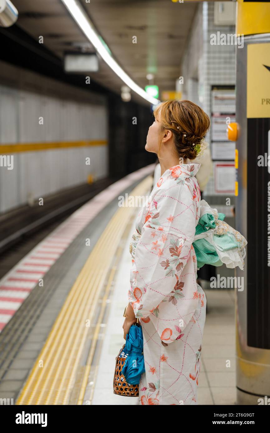 Porträt einer jungen Frau mit japanischem Yukata-Sommerkimono, die auf dem Bahnsteig steht und auf den Zug wartet. Kyoto, Japan. Stockfoto