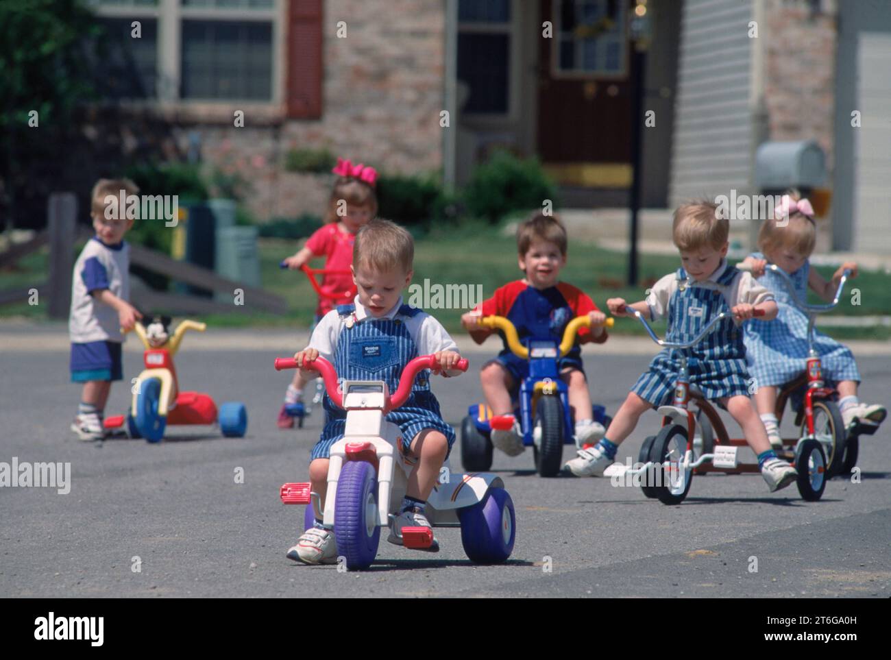 Drei Jahre alte Sextuplets fahren Dreiräder die Straße runter. Stockfoto