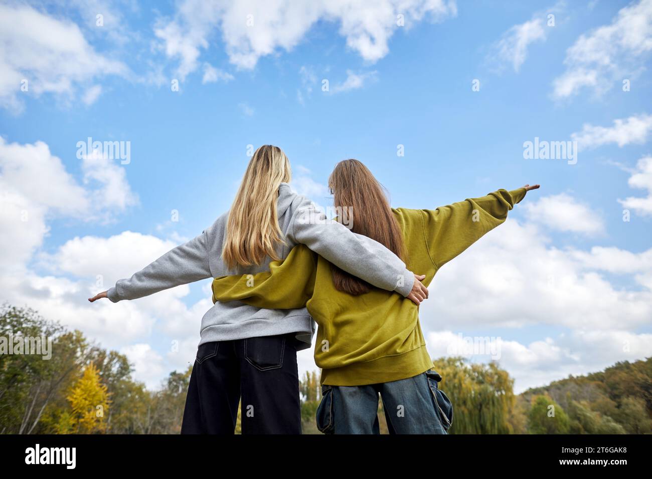 Rückansicht junger Mädchen, die sich umarmen und gegen den Himmel stehen Stockfoto