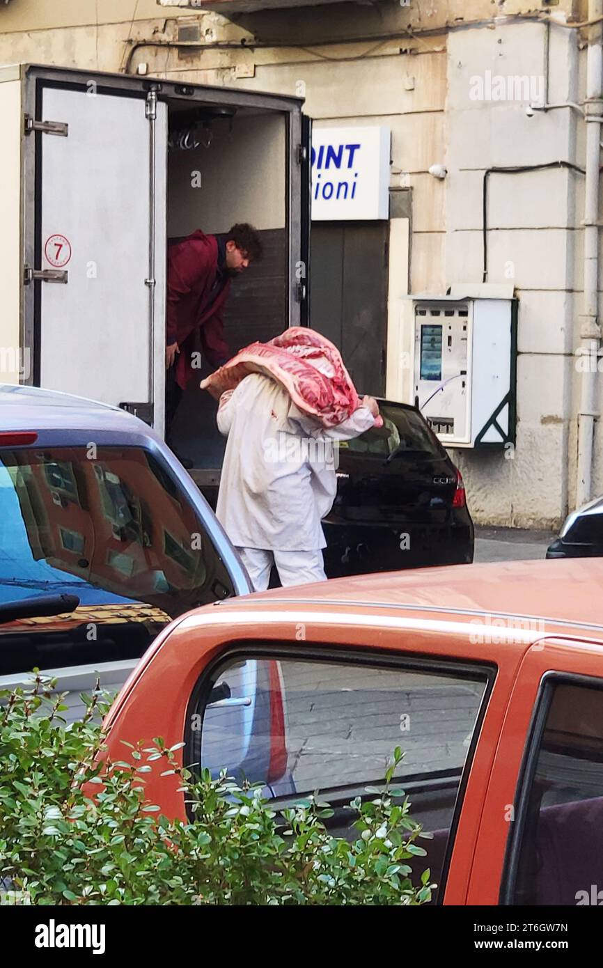 Fleisch kommt in der Innenstadt an, um die Metzgerei zu besuchen, zwei Männer laden Fleisch für eine Metzgerei in den Straßen der Innenstadt von Neapel, Italien. Stockfoto