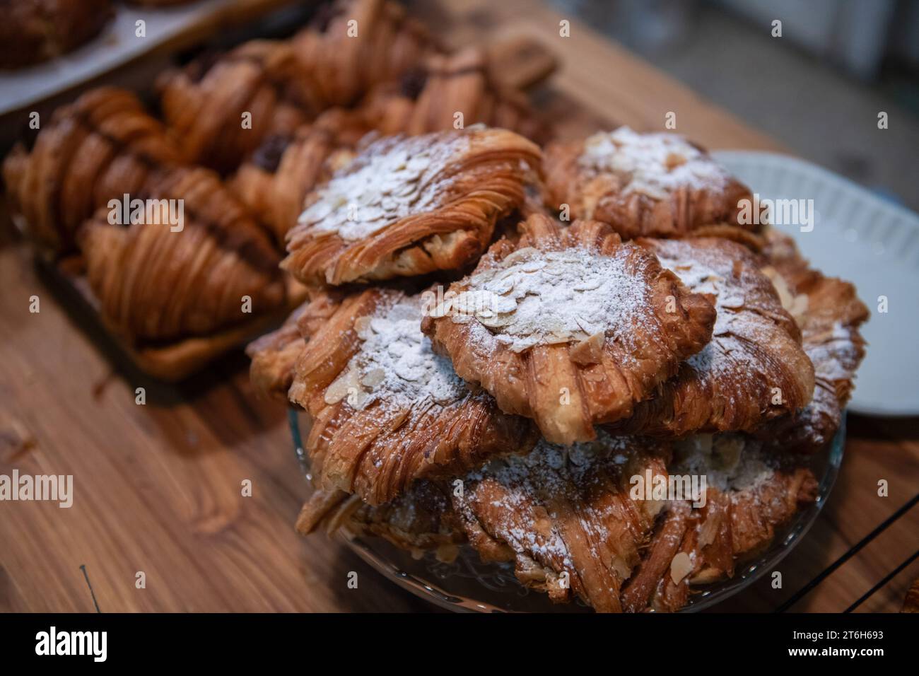 Hausgemachtes Croissant mit Mandelscheiben auf Glas und auf Holzhintergrund im Café, Bäckerei-Konzept Stockfoto