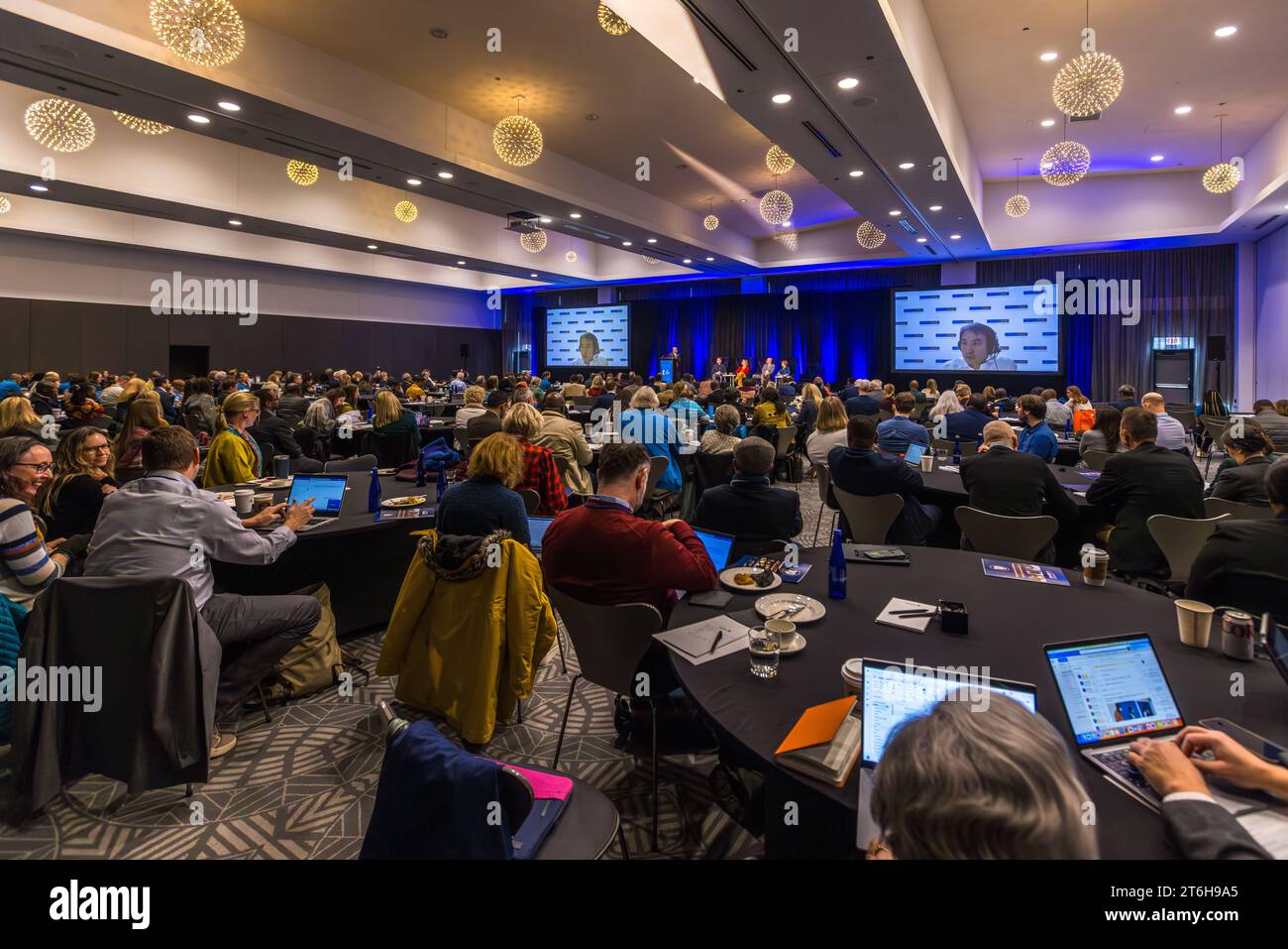 Zahlreiche Teilnehmer verfolgen eine Präsentation im Ballsaal des Radisson Blu Aqua Hotel in Chicago, Illinois, USA, zwei große Bildschirme zeigen Porträtaufnahmen vom Podium. Das Hotel befindet sich in den unteren Etagen des Aqua Tower, der 2009 von der Architektin Jeanne Gang entworfen wurde. Stockfoto