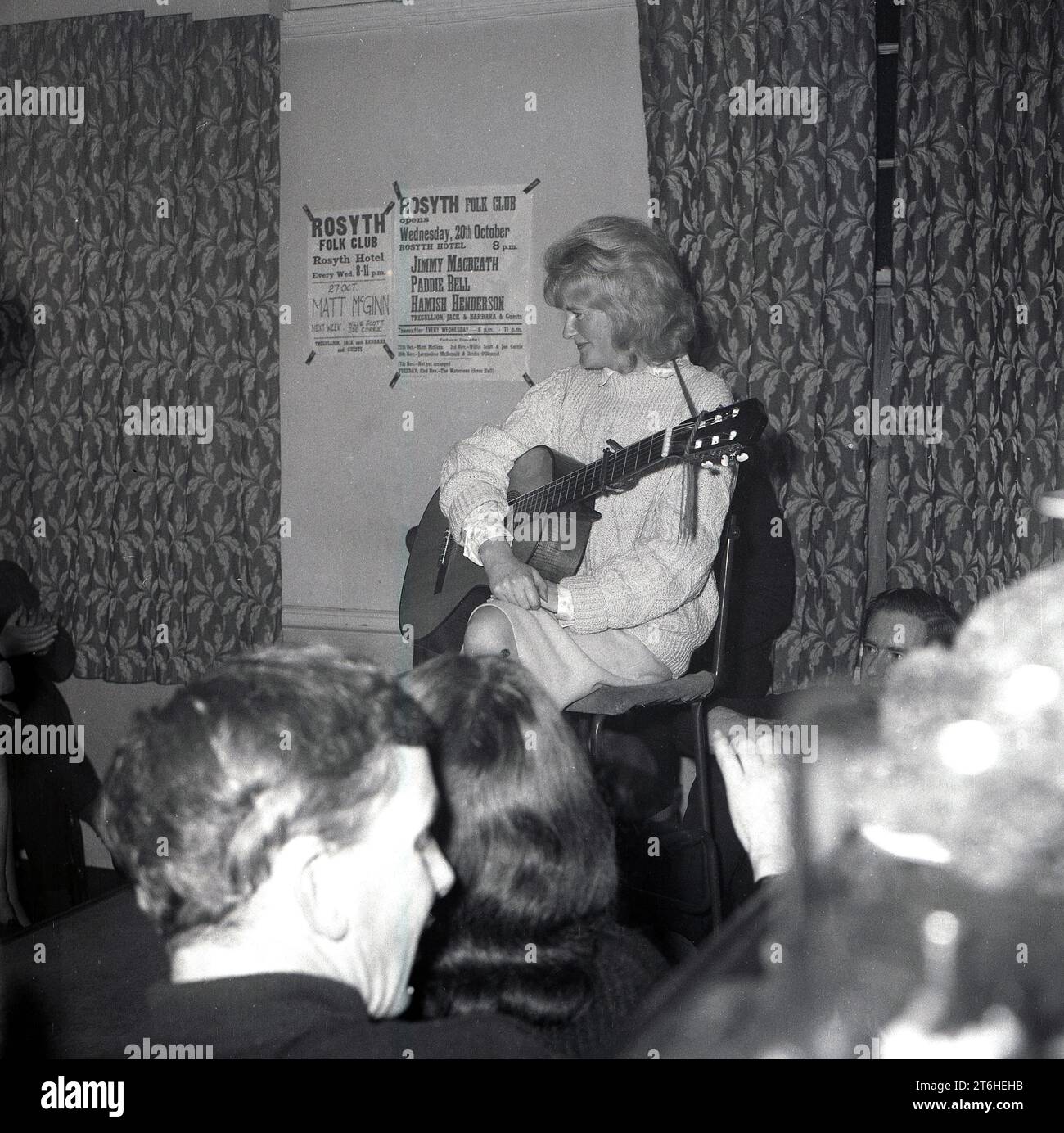 Etwa Ende der 1960er Jahre, historisch, eine weibliche Folk-Sängerin, die in einem Raum mit Gitarre sitzt. An der Wand hinter ihr festgeklemmt, werden die Sänger Jimmy Macbeath, Paddie Bell, Hamish Henderson am 20. Oktober mit Tregullion Jack & Barbara & Guests und Matt McGinn aufgeführt. Stockfoto