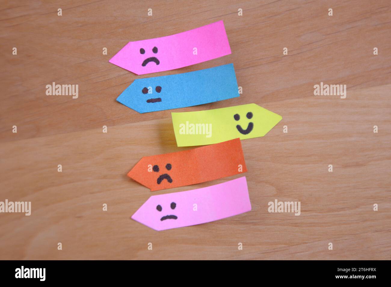 Positiver Smiley glänzt unter traurigen Gesichtern auf Haftnotizen. Positivitätskonzept Beibehalten. Traurigkeit mit Positivität überwinden. Stockfoto