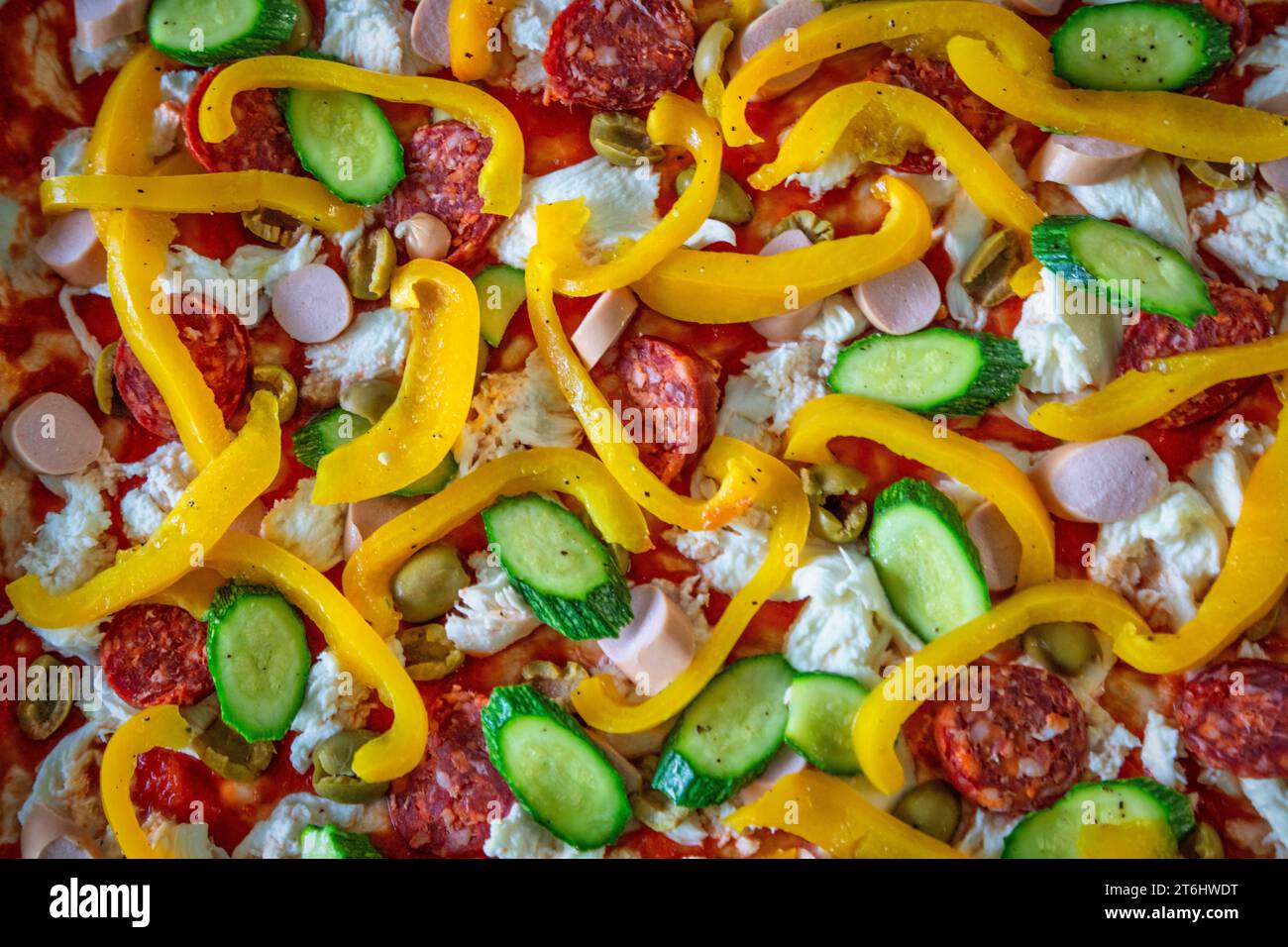 Hausgemachte italienische Pizza, bevor sie im Ofen gekocht wird, gefüllt mit Tomaten, Mozzarella, Paprika, Zucchini, Frankfurters und scharfe Salami Stockfoto