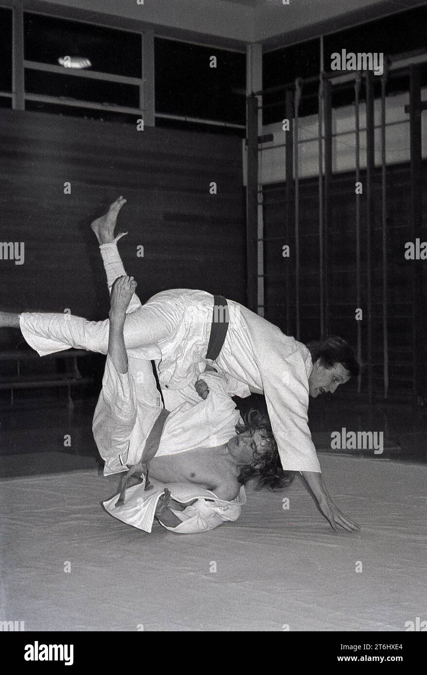 1970er Jahre, Judo, männliche Konkurrenten, die sich auf einer Matte in einer Sporthalle auseinandersetzen. Die japanische Kampfkunst des Judo ist eine harte körperliche Sportart, die zahlreiche Züge umfasst, aber auch eine starke geistige Disziplin, Konzentration und Belastbarkeit erfordert. Ein wichtiger Faktor im Judo ist der Respekt für deinen Gegner und dich selbst. Stockfoto