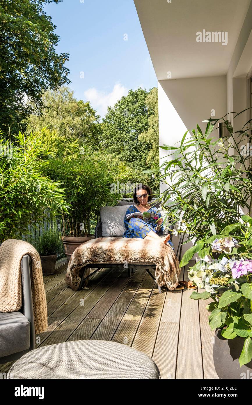 Frau, die auf dem Balkon sitzt und mit modernen Lounge-Möbeln eine Zeitschrift liest, Stockfoto