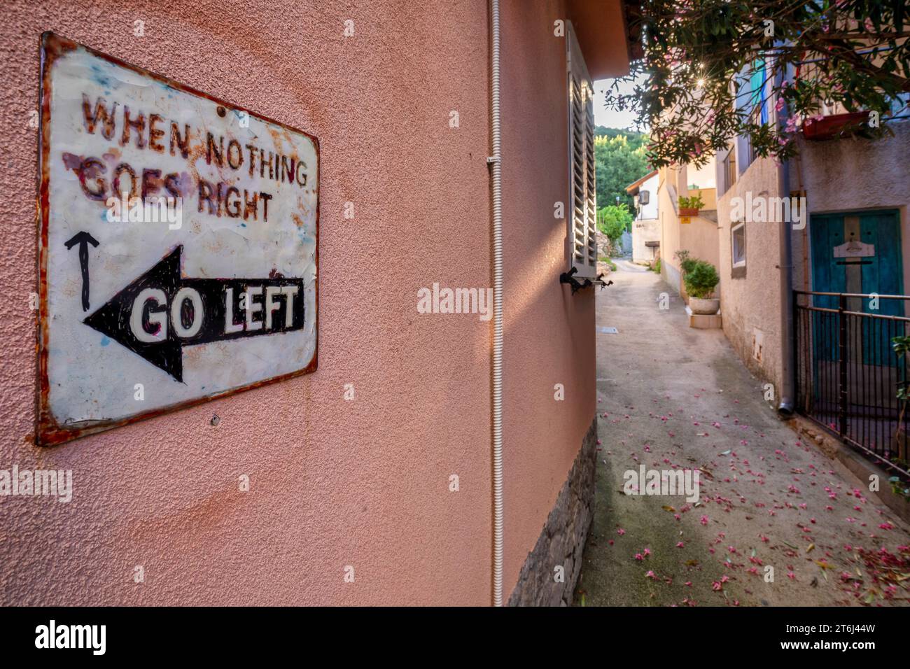Vintage-Richtungstafel hängt an einer pinkfarbenen Wand mit lustigem Schriftzug „When Nothing Goes Right Go Left“ Stockfoto
