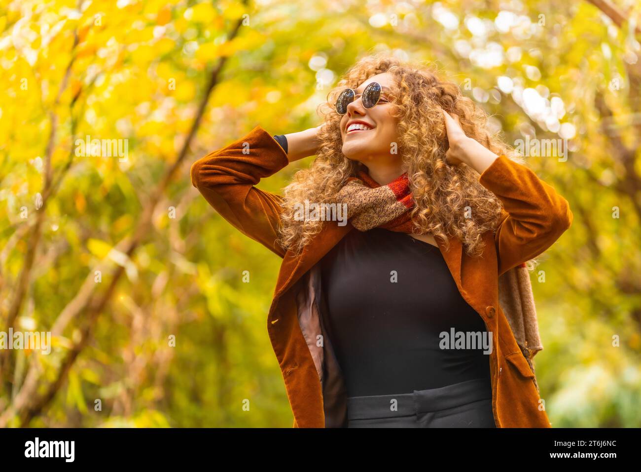 Frau mit Sonnenbrille und lässiger Kleidung, die im Herbst in einem Park aufblickt Stockfoto