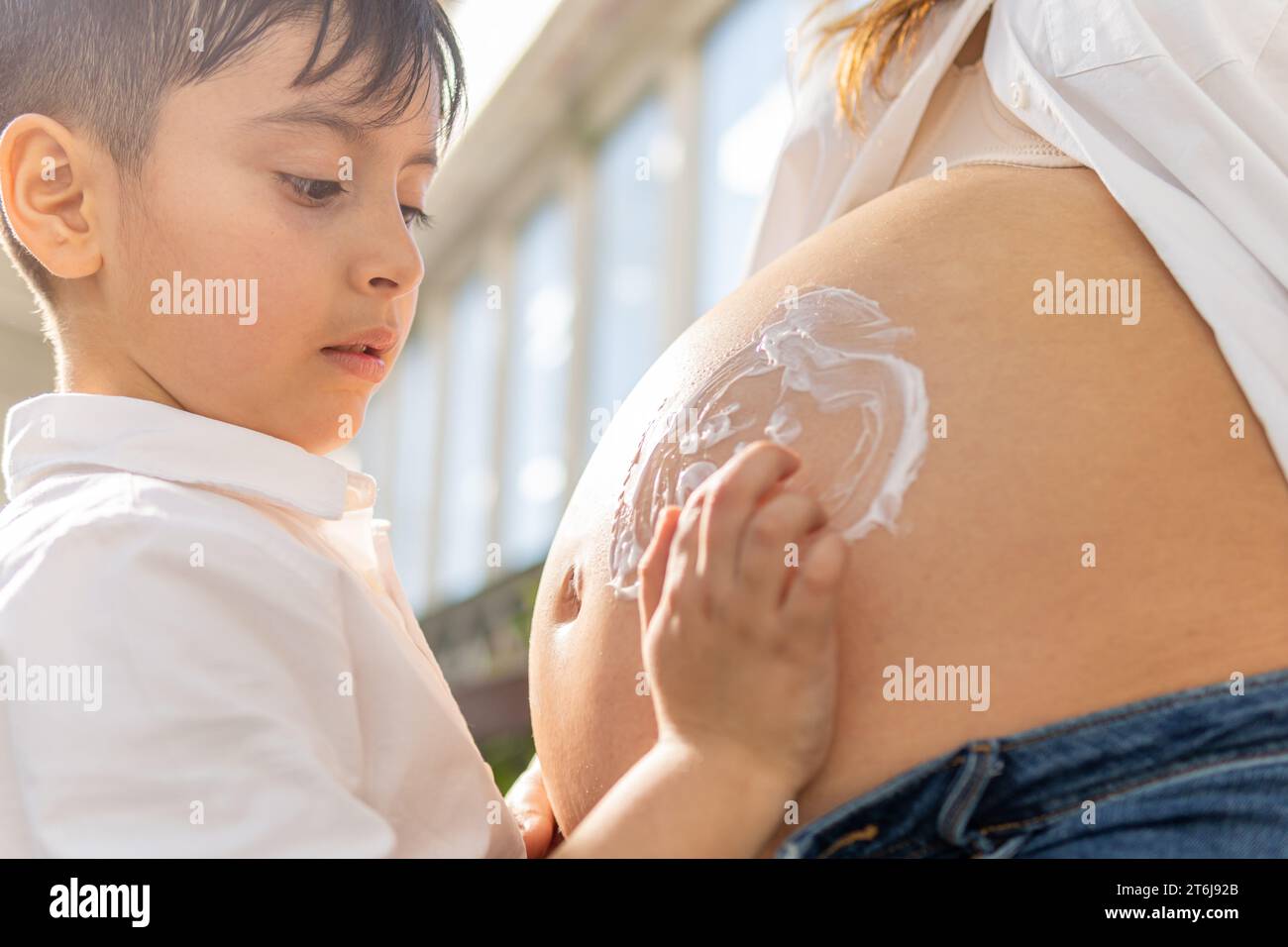 Junge, der Emoji mit Mosturizer auf dem Bauch der schwangeren Frau zeichnet Stockfoto