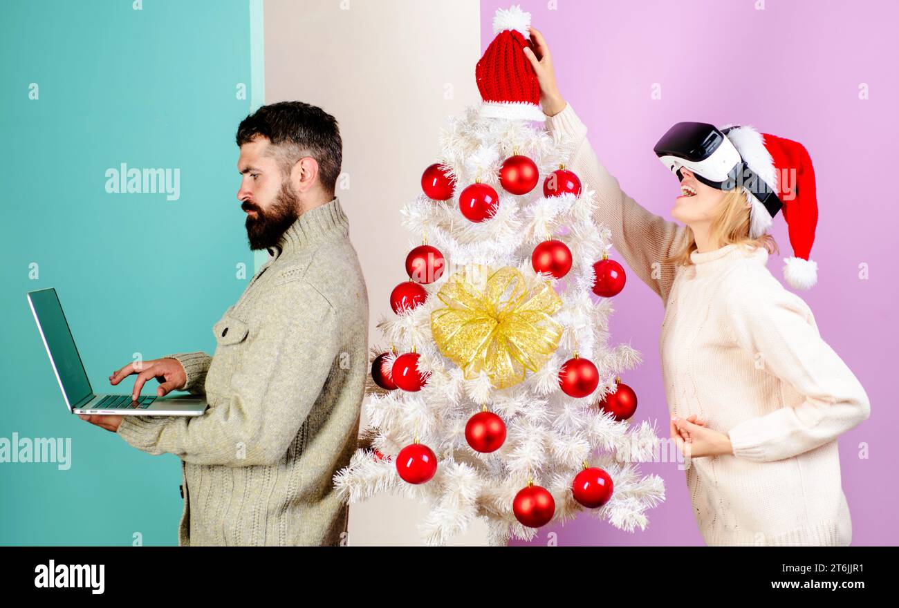 Moderne Technologie. Bärtiger Mann mit Laptop und lächelndem Mädchen mit Weihnachtsmütze in VR-Brille. 3D-Technologie, Unterhaltung. Glückliche Familie in der Nähe des Weihnachtsbaums Stockfoto