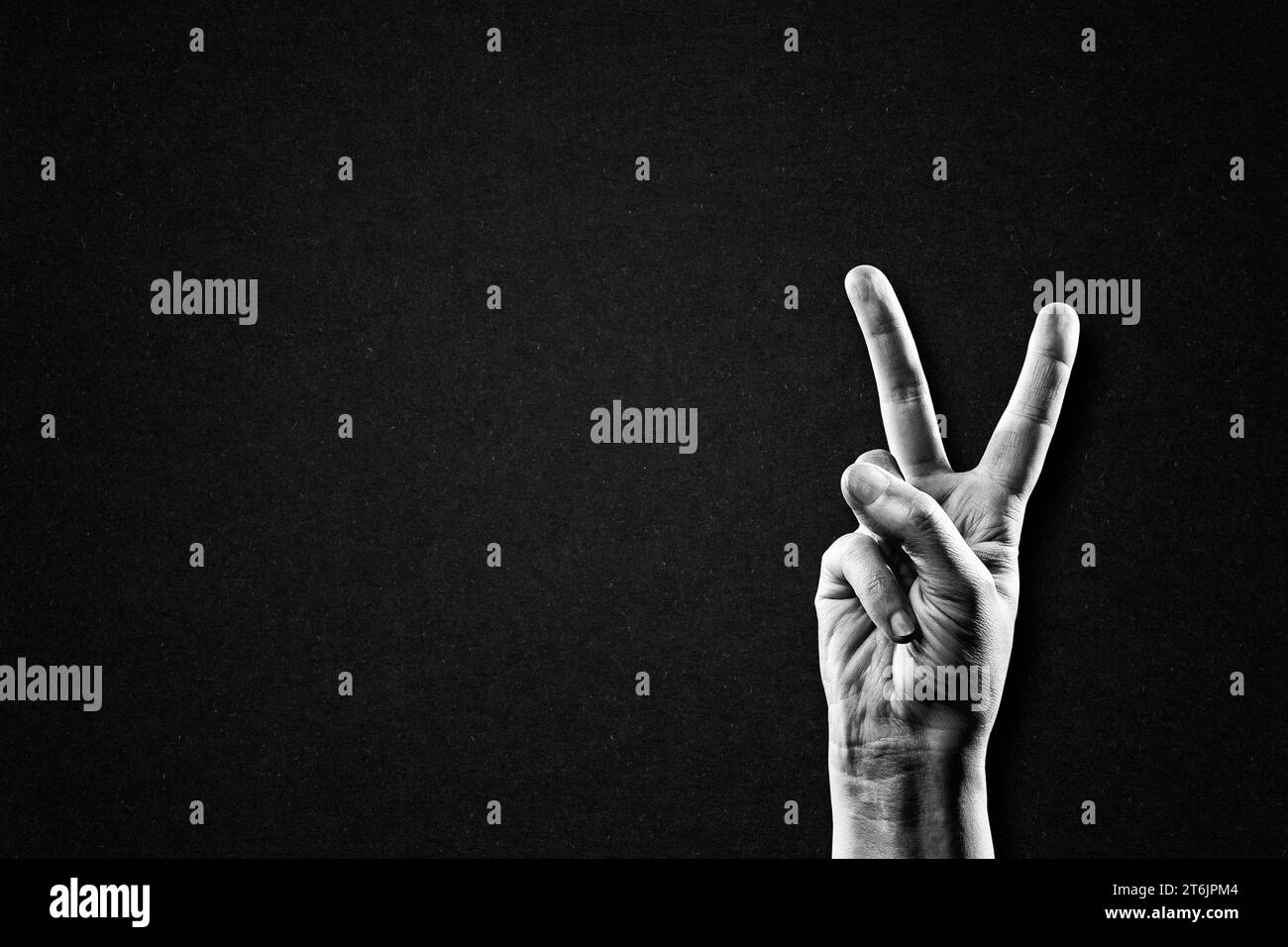 Hand zeigt Friedenssieg-Zeichen in Schwarz-weiß auf strukturiertem Papierhintergrund, Kopierraum Stockfoto