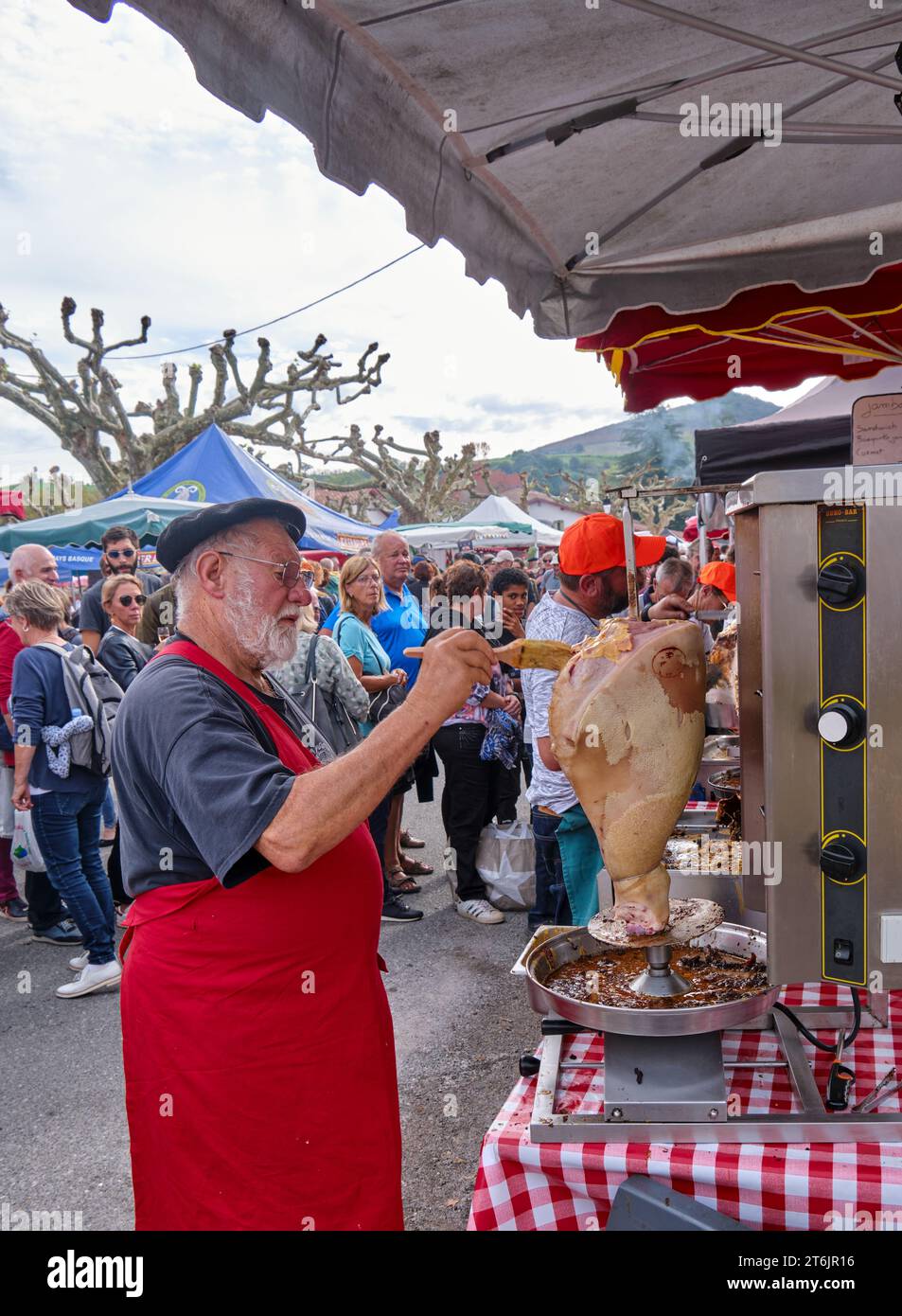 Baskenmütze und rote Schürze würzen auf dem Markt in Espelette, Frankreich, während des jährlichen Pfefferfestivals ein großes Stück Fleisch Stockfoto