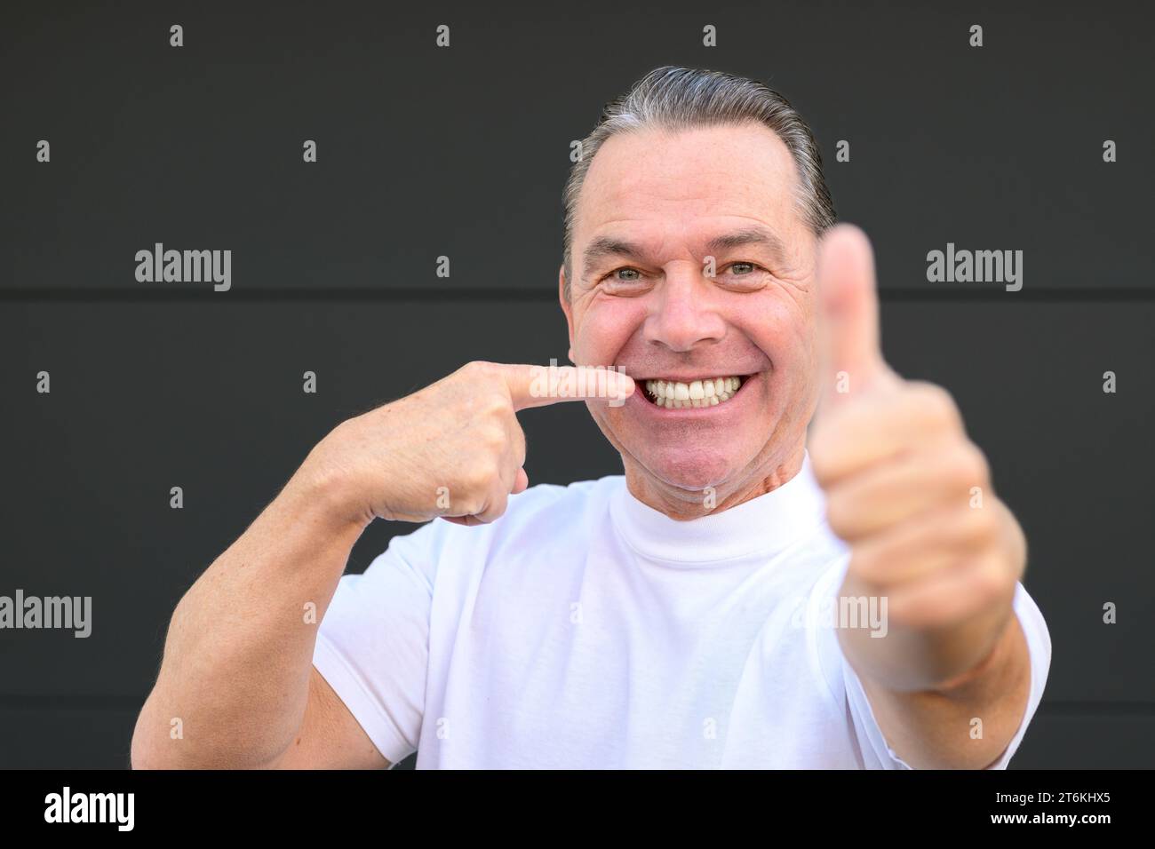 Ein Mann mit einem großen Lächeln zeigt auf die Zähne, weil das der beste Zahnarzt der Stadt war Stockfoto