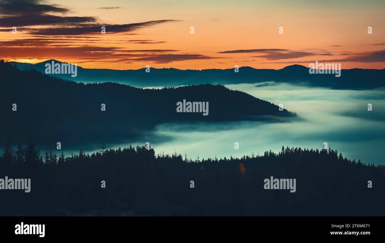 Sonnenaufgangsmeer aus Nebel, der sich über die Silhouette der Bergkette bewegt, mit Blick auf den Kiefernwald aus der Vogelperspektive. Wilde Natur Nebellandschaft. Dramatische dunkle Wolken schweben im orangefarbenen Himmel Stockfoto