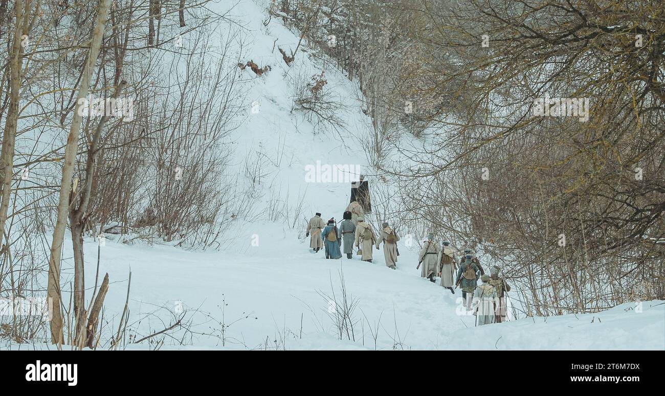 Als Soldaten der Weißen Garde verkleidete Männer der kaiserlichen russischen Armee im russischen Bürgerkrieg, die durch den schneebedeckten Winterwald marschieren. Historische Nachstellung von Stockfoto
