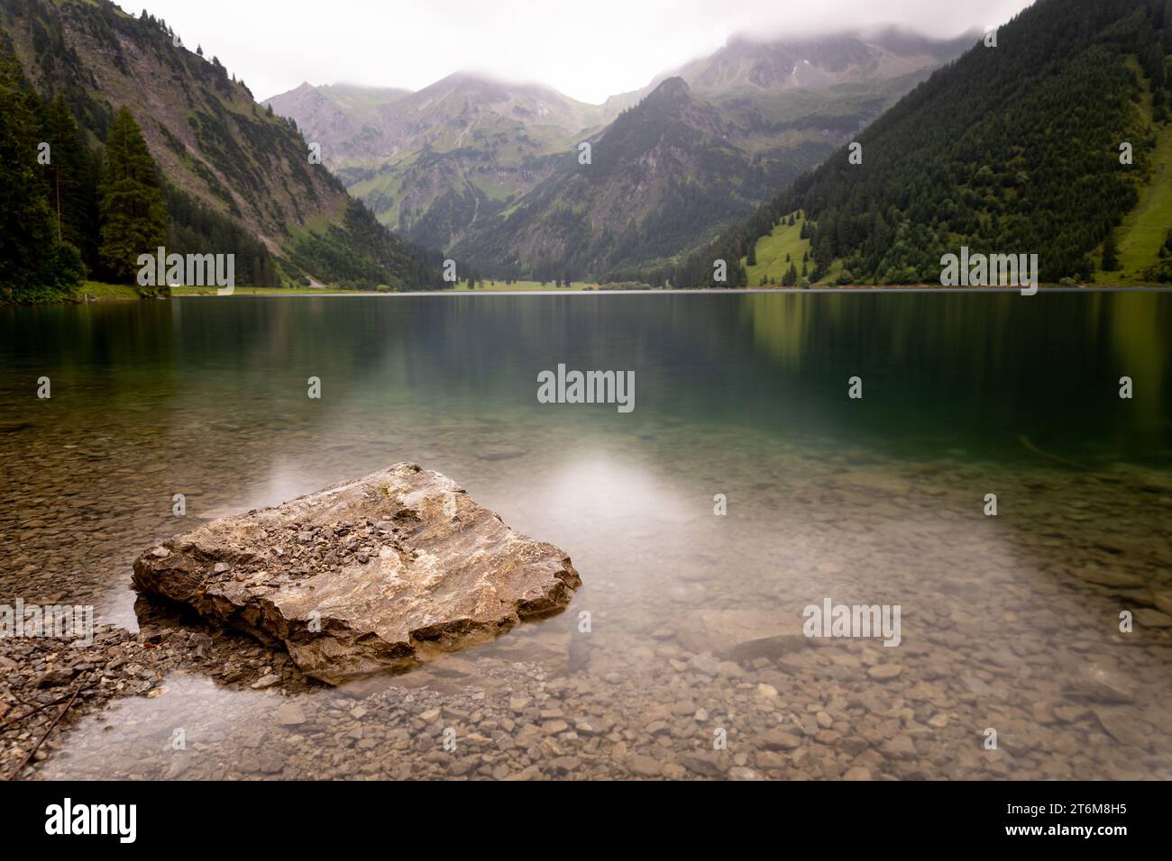 Felsen im Bergsee mit kristallklarem Wasser, glatter Oberfläche und leicht verschwommenem Hintergrund im Vilsalpsee der österreichischen alpen Stockfoto