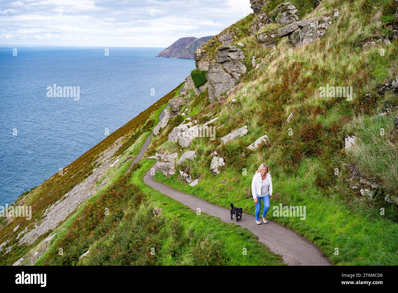 Eine Dame, die mit einem Hund auf dem Southwest Coast Path im Valley of Rocks bei Lynton, Devon, Großbritannien, unterwegs ist. Stockfoto