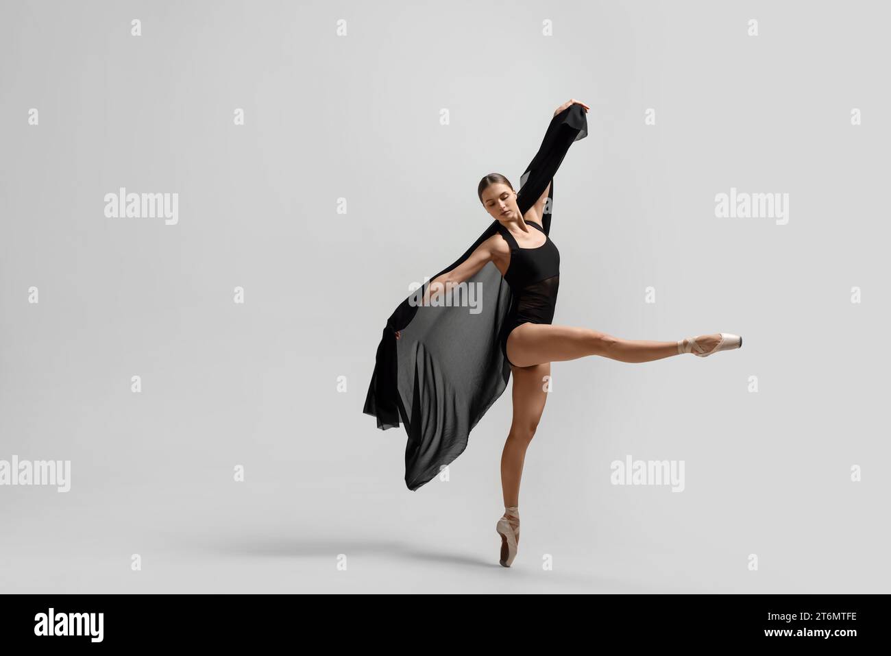 Anmutige junge Ballerina, die Tanzbewegungen mit schwarzem Schleier auf weißem Hintergrund praktiziert Stockfoto