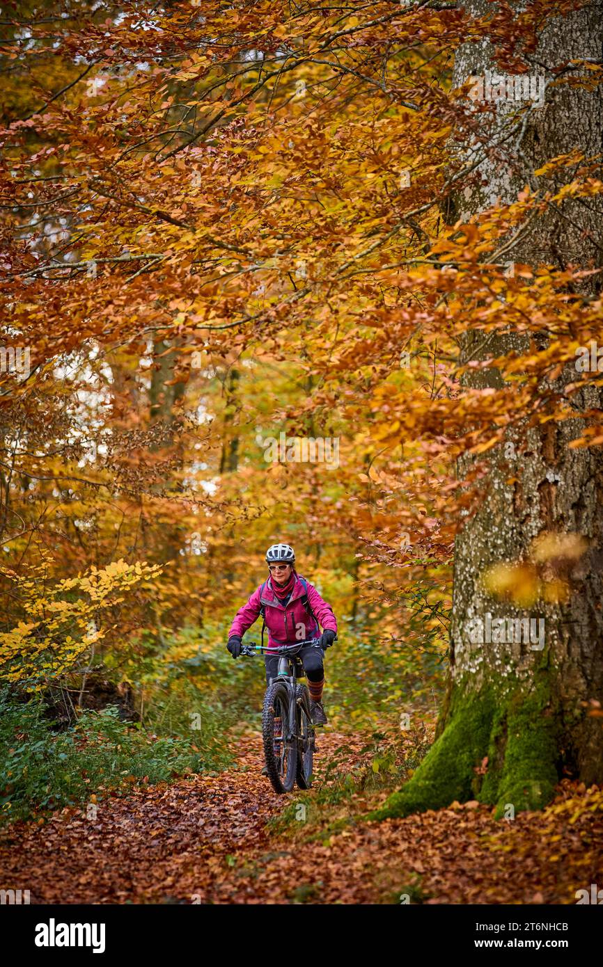 Nette Seniorin, die ihr E-Mountainbike auf den herbstlichen Waldwegen in der Nähe von Stuttgart, Baden-Württemberg, fährt Stockfoto